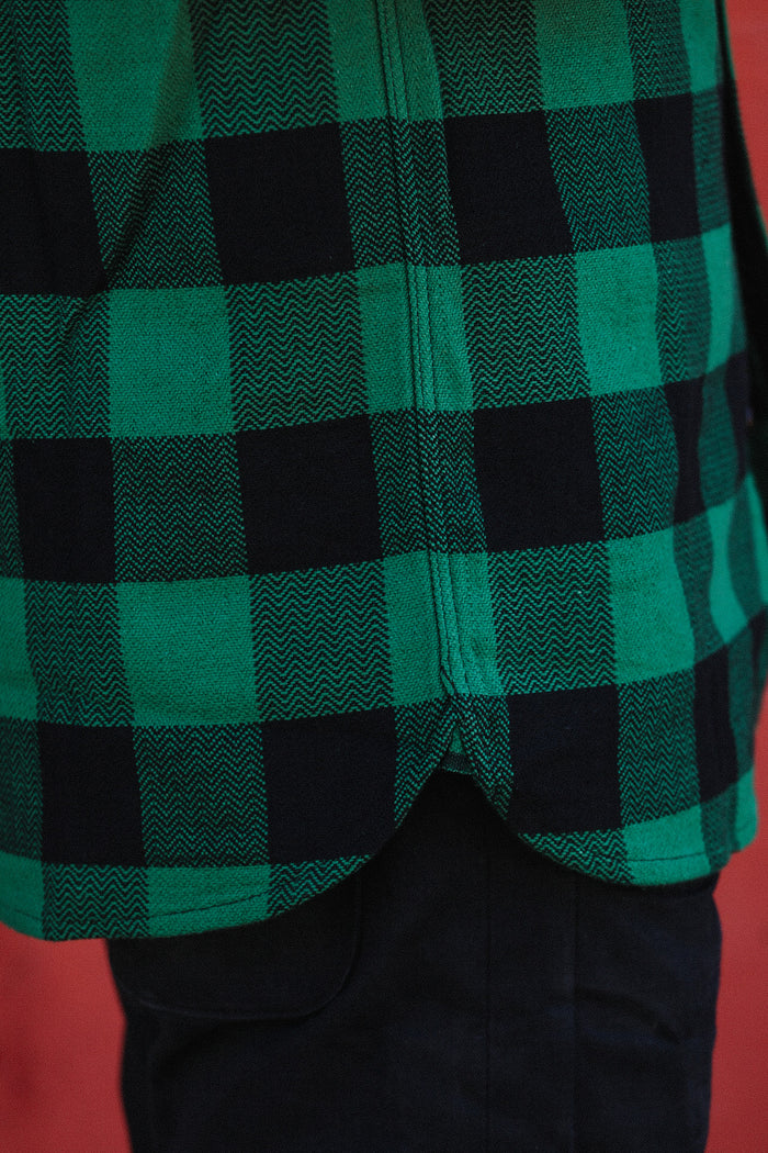 Close-up of green and black checkered flannel shirt hem over dark pants on red background