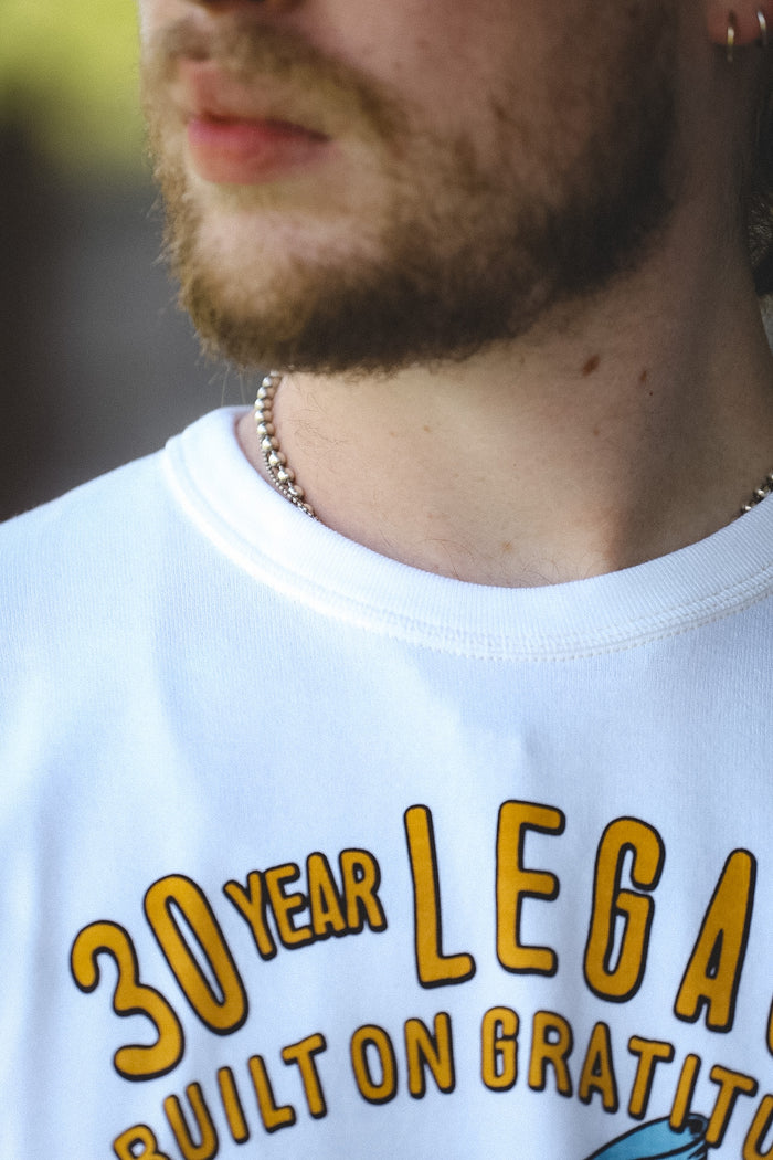 Close-up of a man wearing a white graphic t-shirt with yellow text that reads '30 YEAR LEGAL BUILT ON GRATITUDE'.