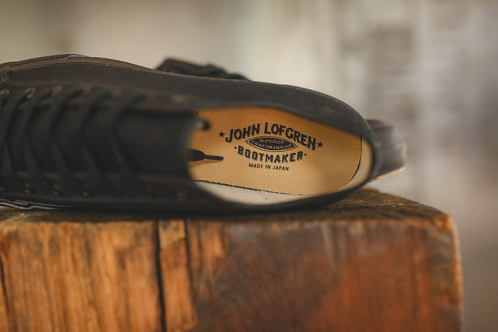 Up close image of a black sneaker on a wood block with a grey background