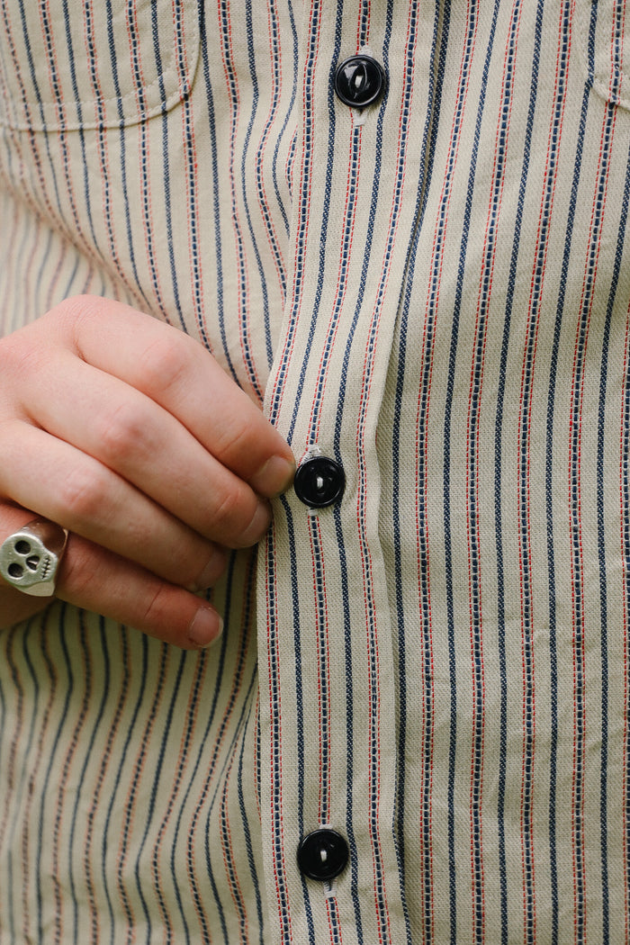 Close-up of a person buttoning a striped shirt with a hand wearing a skull ring.