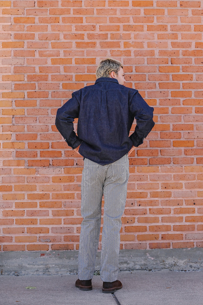 Man wearing navy blue shirt and striped pants standing with back to brick wall