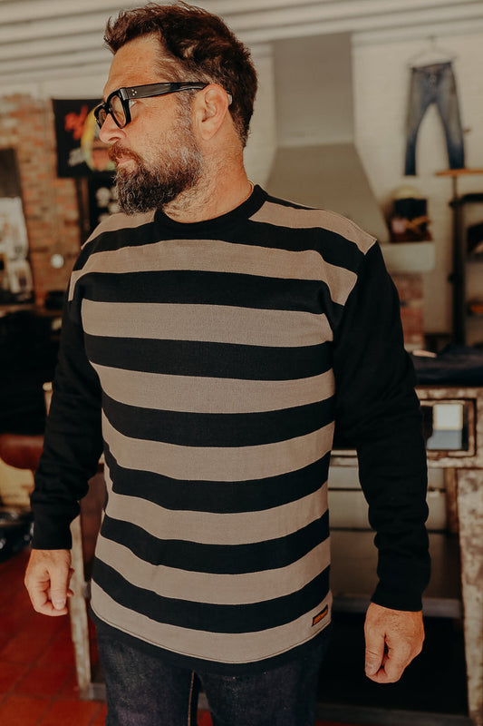 Bearded man wearing black and brown striped long sleeve shirt in rustic indoor setting at Iron Shop Provisions