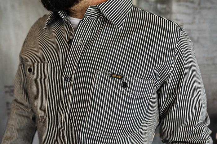 Close-up of a man wearing a black and white striped Iron Heart work shirt with buttoned chest pockets