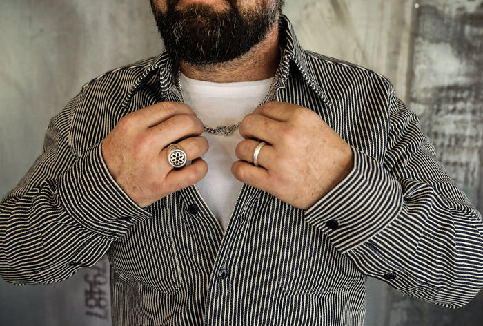 Bearded man wearing striped jacket and white shirt adjusting silver chain necklace with rings