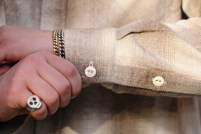 Close-up of a person wearing a beige shirt with buttons and a bracelet.