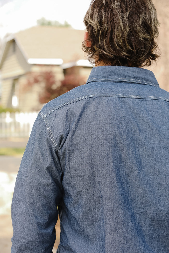 Person wearing a blue denim shirt with a blurred outdoor background