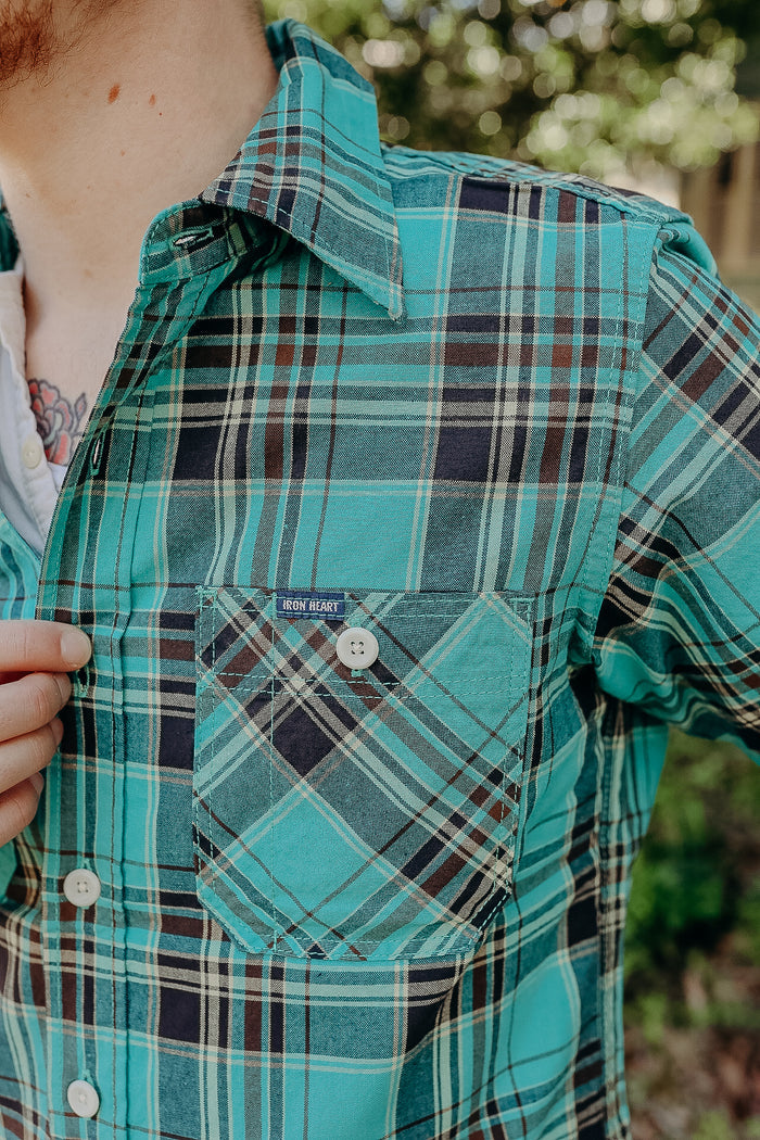 Close-up of teal and navy plaid Iron Heart button-up shirt with pocket detail worn outdoors