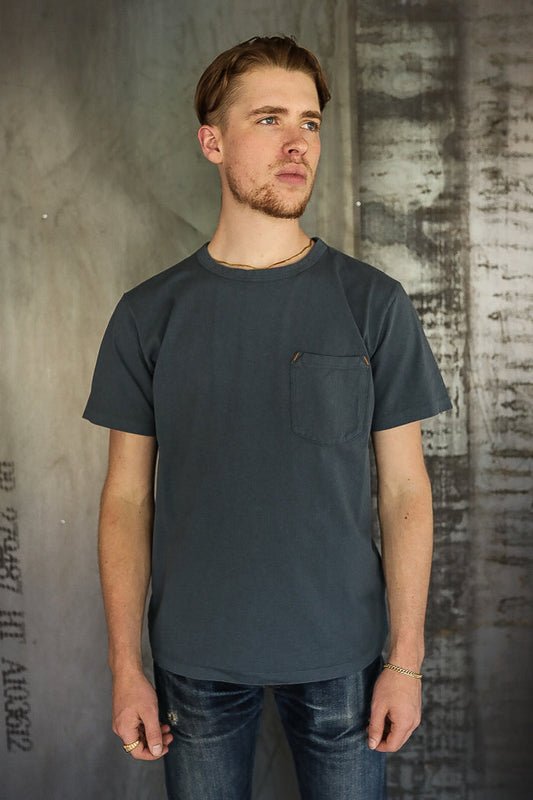 Young man wearing dark gray pocket t-shirt and distressed jeans in industrial setting