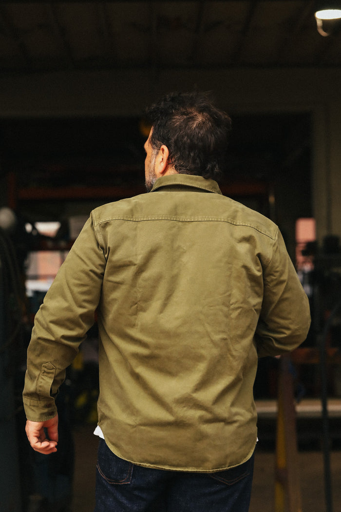 Man wearing a green jacket walking away in an indoor setting