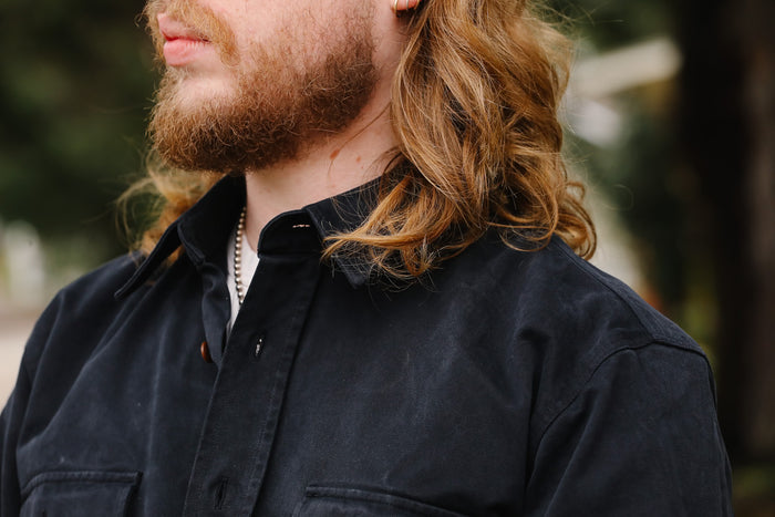 Man with long hair and beard wearing a dark jacket outdoors