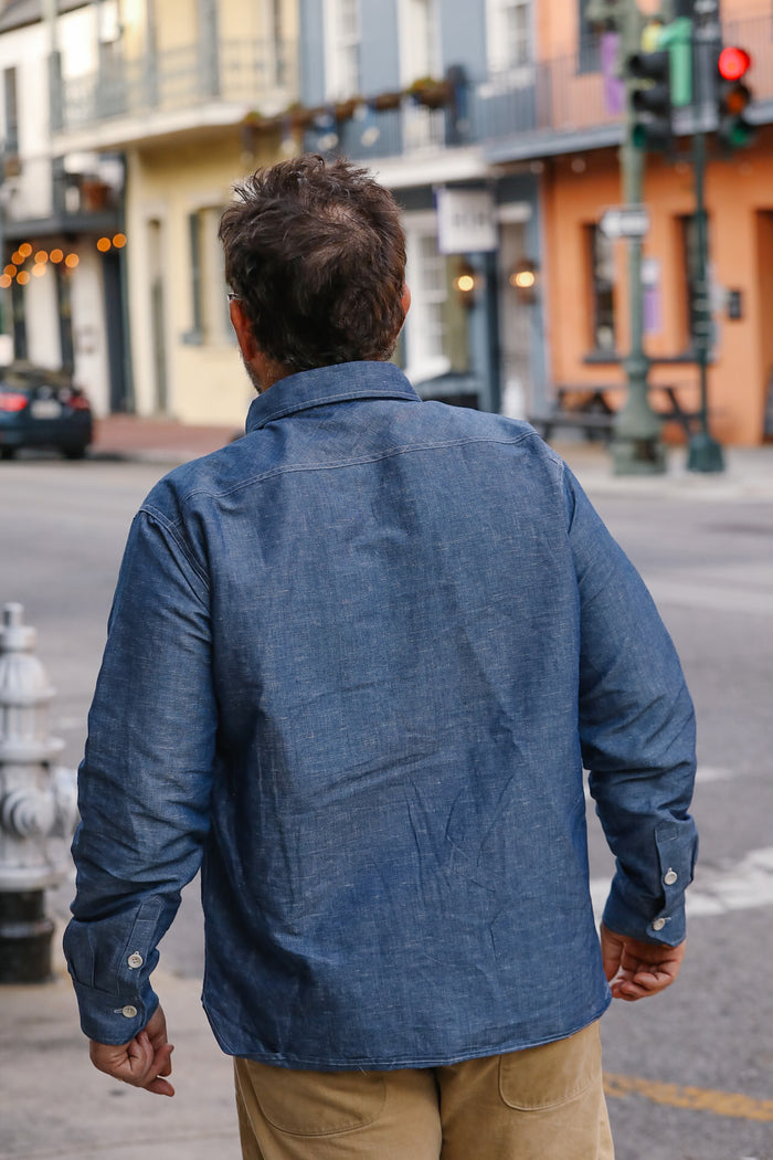 Man wearing a blue denim jacket walking on a city street.