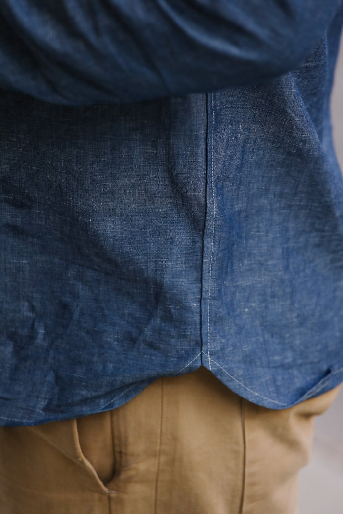 Close-up of a person wearing a blue denim shirt and beige pants.
