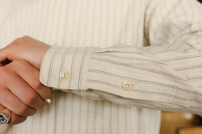 Close-up of a person wearing a beige striped shirt with rolled-up sleeves.