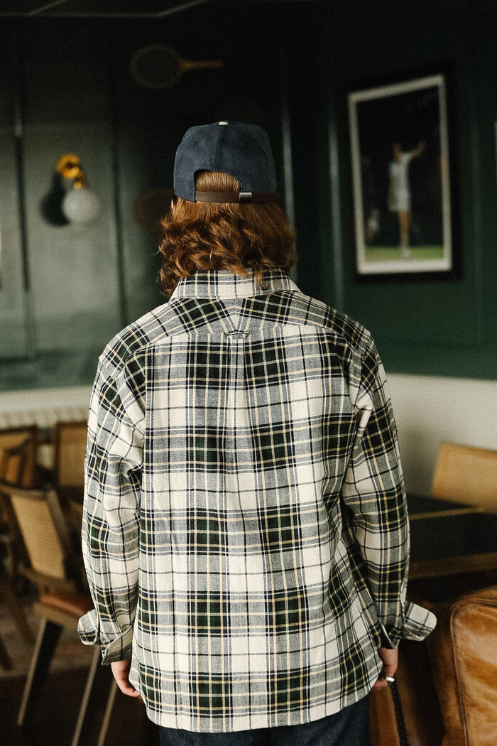 Person wearing a plaid shirt and cap in a room with chairs and a wall-mounted light fixture.