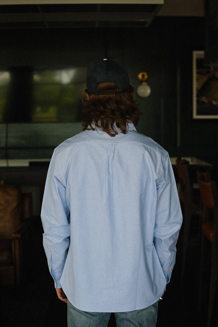 Person wearing a light blue shirt and dark cap in a dimly lit room.