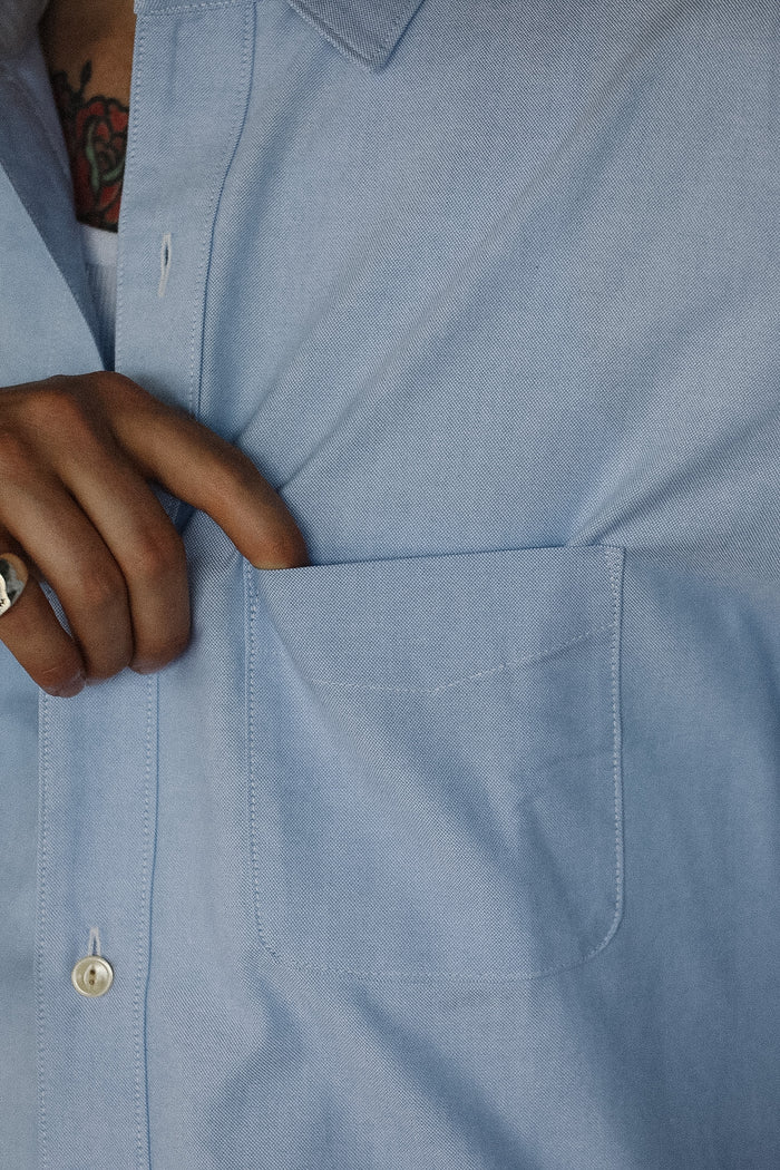 Close-up of a person wearing a light blue shirt with a hand adjusting the collar.