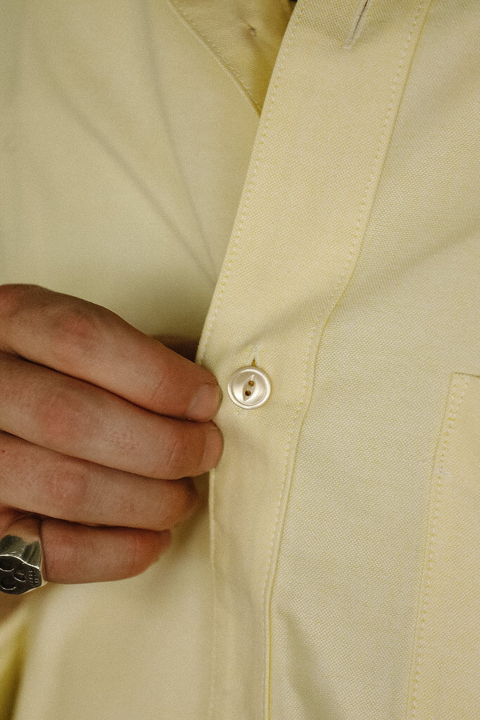 Close-up of a beige jacket with a button being pressed, wearing a ring.