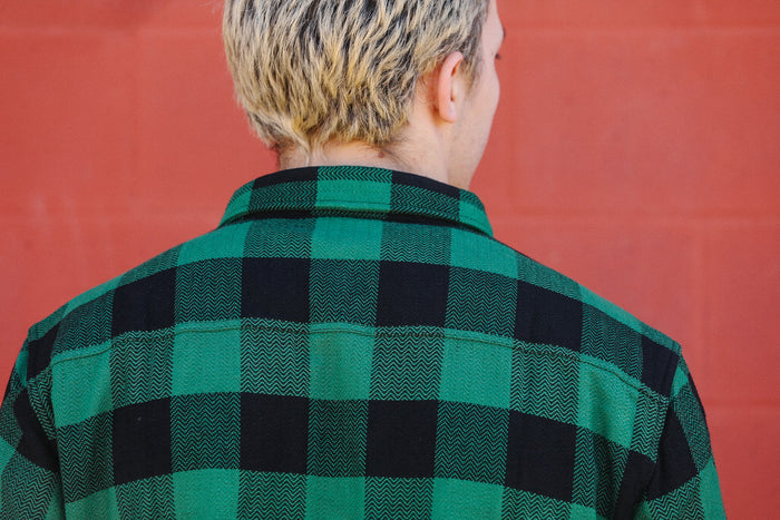 Back view of person wearing green and black checkered flannel shirt against red brick wall