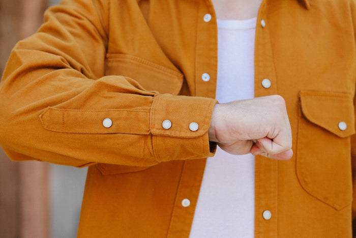 Close-up of a person wearing a rust orange button-up work shirt over a white shirt at Iron Shop Provisions