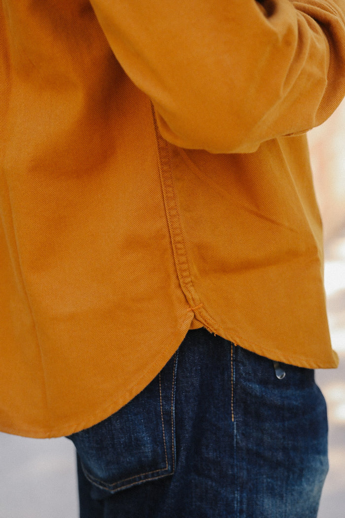 Close-up of orange work shirt hem and blue denim jeans pocket detail