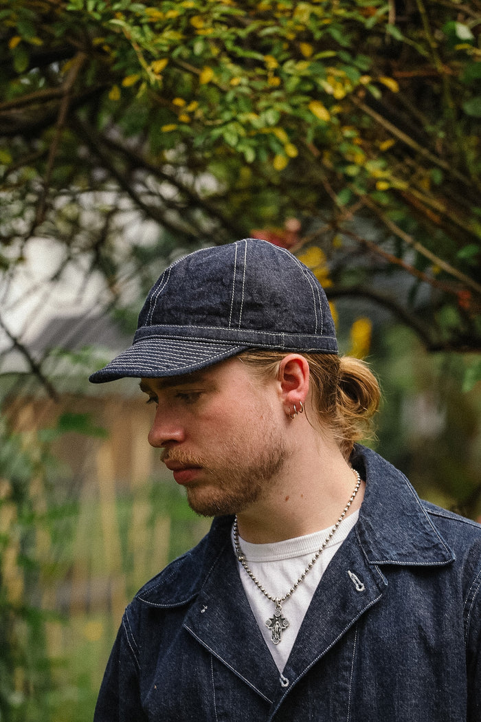 Man wearing a denim cap and coat outdoors with trees in the background