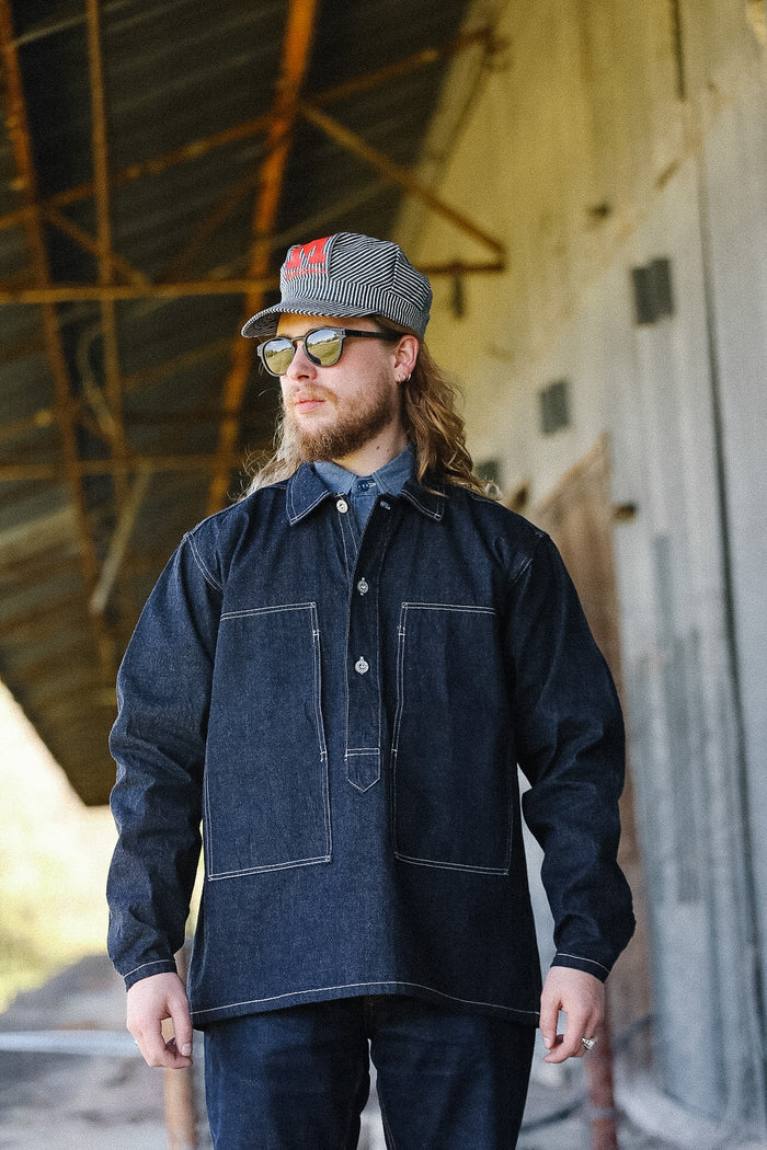 Man wearing a denim jacket and cap standing in an industrial setting