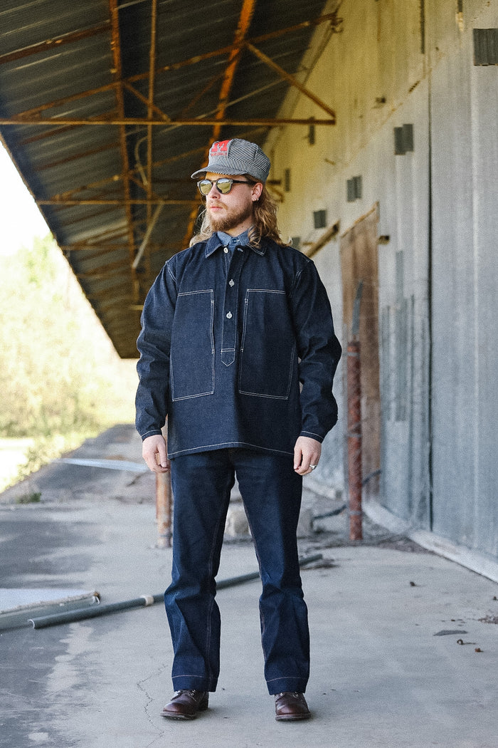 Man wearing a denim jacket and jeans standing in an industrial setting