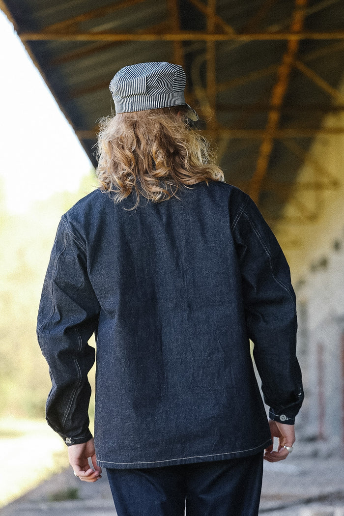 Person wearing a dark denim jacket and cap from behind, standing under a rustic wooden structure.