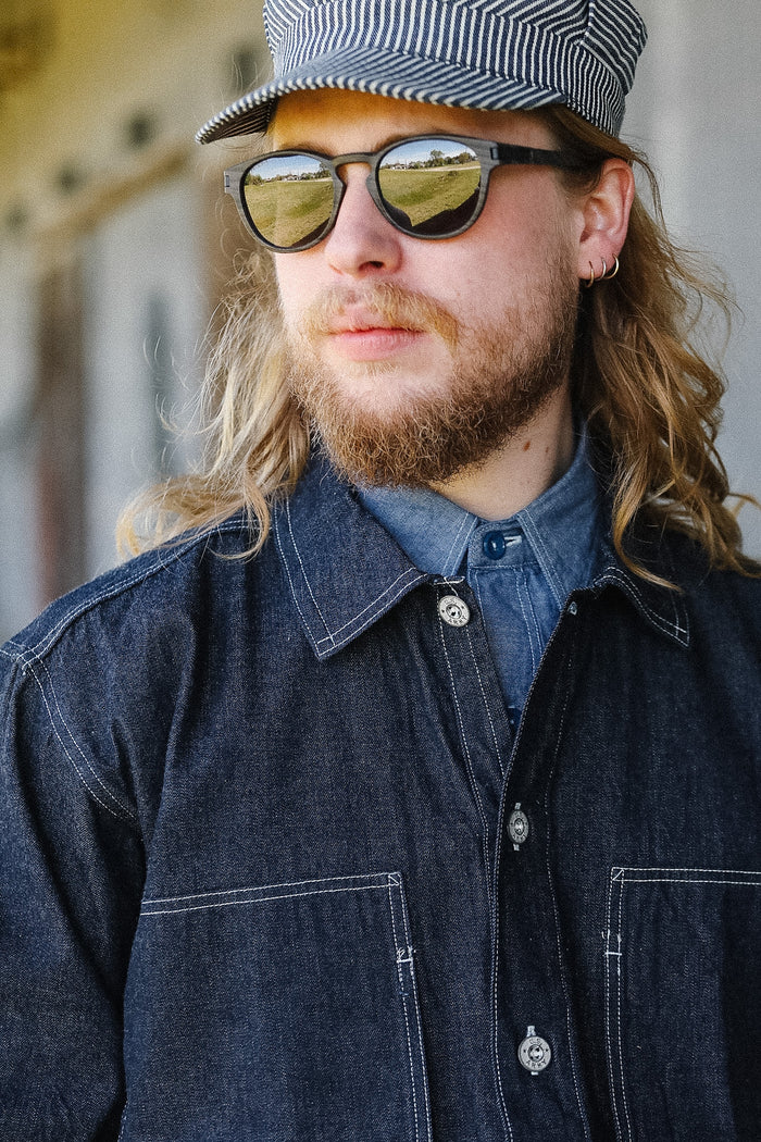 Man wearing a denim jacket, striped cap, and sunglasses with a blurred background