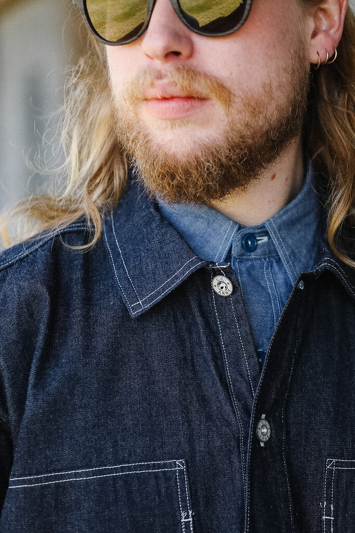 Man wearing sunglasses and a denim jacket with a blurred background