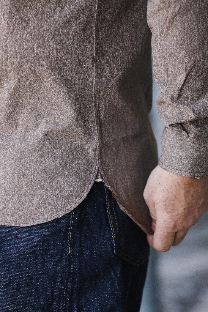 Close-up of a person wearing a brown shirt and dark jeans against a light background