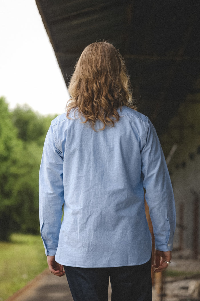 Person wearing a blue shirt standing under a bridge with greenery in the background