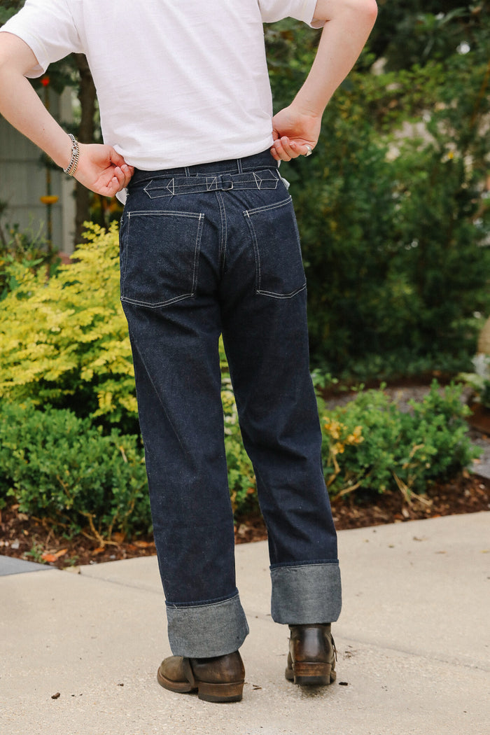Person wearing dark blue jeans and a white shirt outdoors with greenery in the background