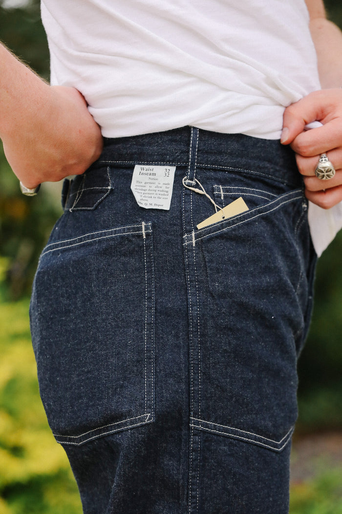 Person wearing dark blue jeans with a visible brand tag, standing outdoors.