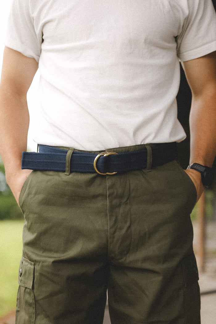 Person wearing a white t-shirt, green pants, and a blue belt with a blurred background
