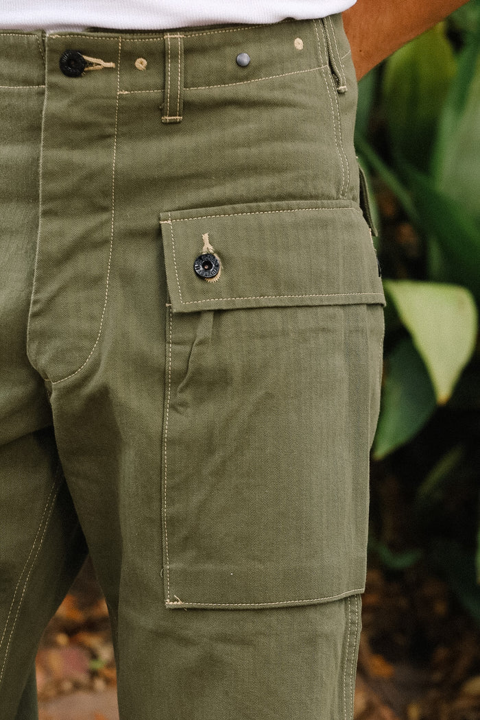 Close-up of green pants with a pocket detail, blurred natural background