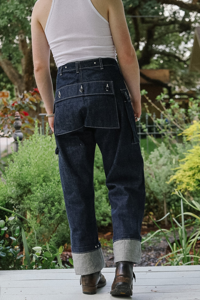 Person wearing dark blue jeans and a white tank top standing in a garden.