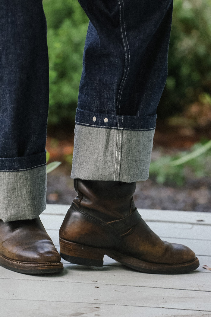 Brown leather boots worn with rolled-up jeans on a wooden floor.
