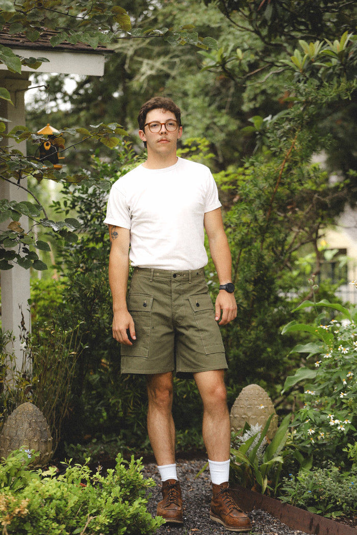 Man standing in a garden wearing a white t-shirt, green shorts, and glasses.