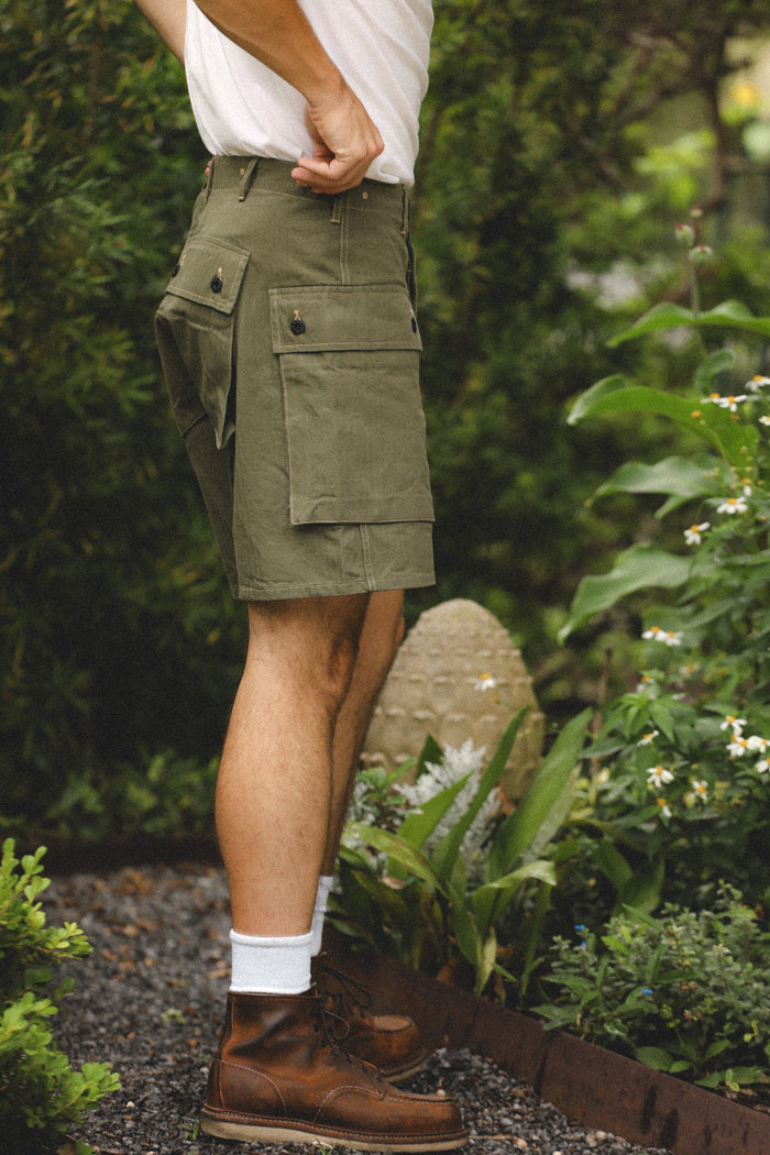 Person wearing green cargo shorts and brown boots in a garden setting
