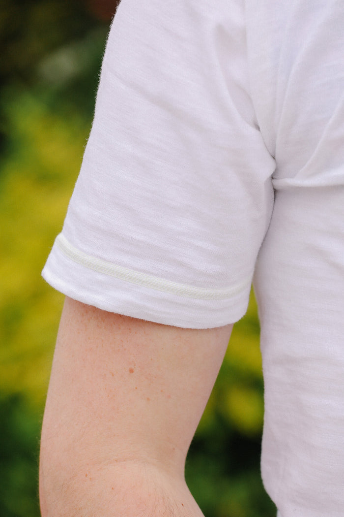 Close-up of a person wearing a light gray t-shirt with rolled-up sleeves against a blurred green background