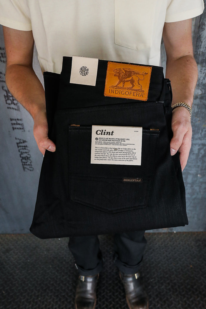 Person holding folded black Indigofera Clint jeans with leather logo patch and white label