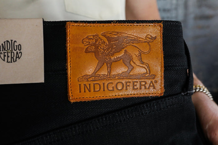 Indigofera black denim jeans with brown leather patch featuring griffin logo and Indigofera branding