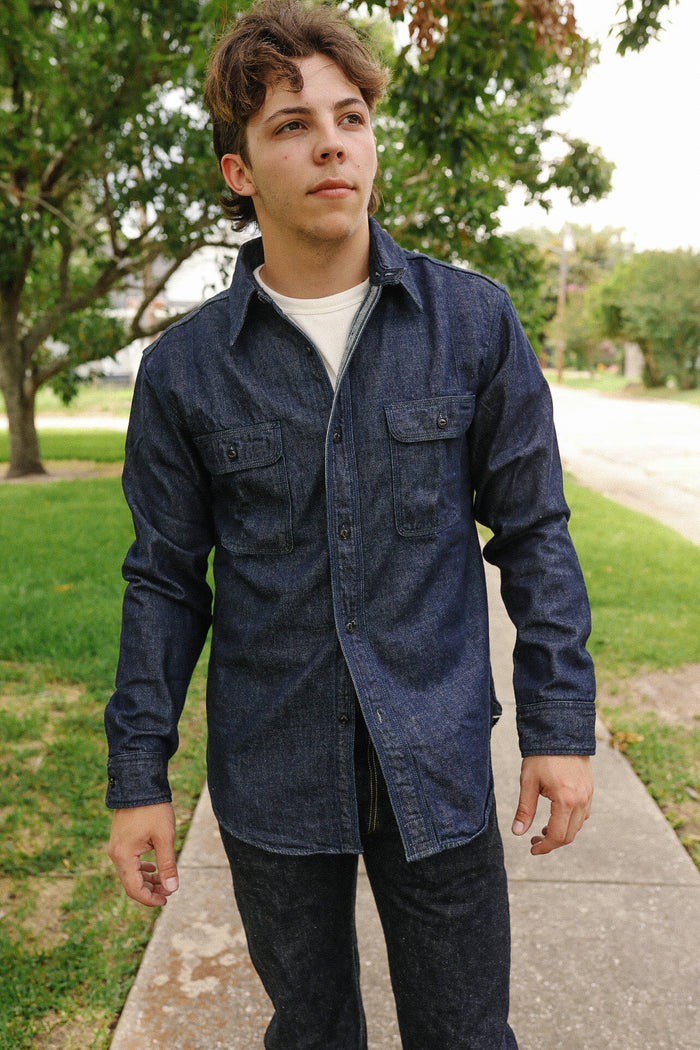 Young man wearing Indigo denim medical shirt with button pockets walking outdoors on sidewalk