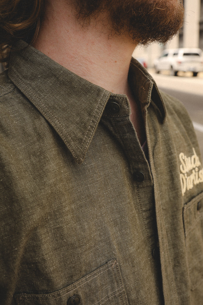 Close-up of a man wearing olive-green button-up shirt with collar and chest pocket in urban setting