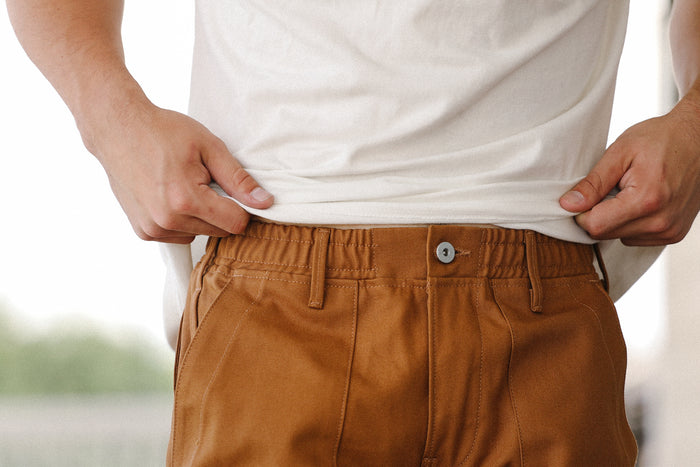 Close-up of man wearing camel canvas fatigue shorts with elastic waistband and white t-shirt