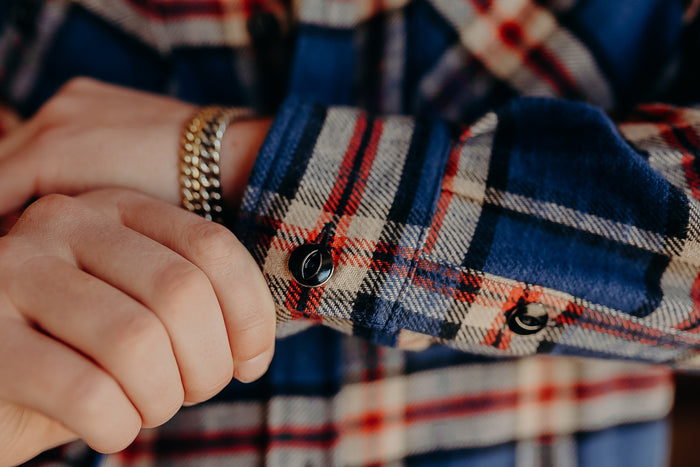 Close-up of hands adjusting sleeve cuff on blue and red plaid shirt with gold chain bracelet