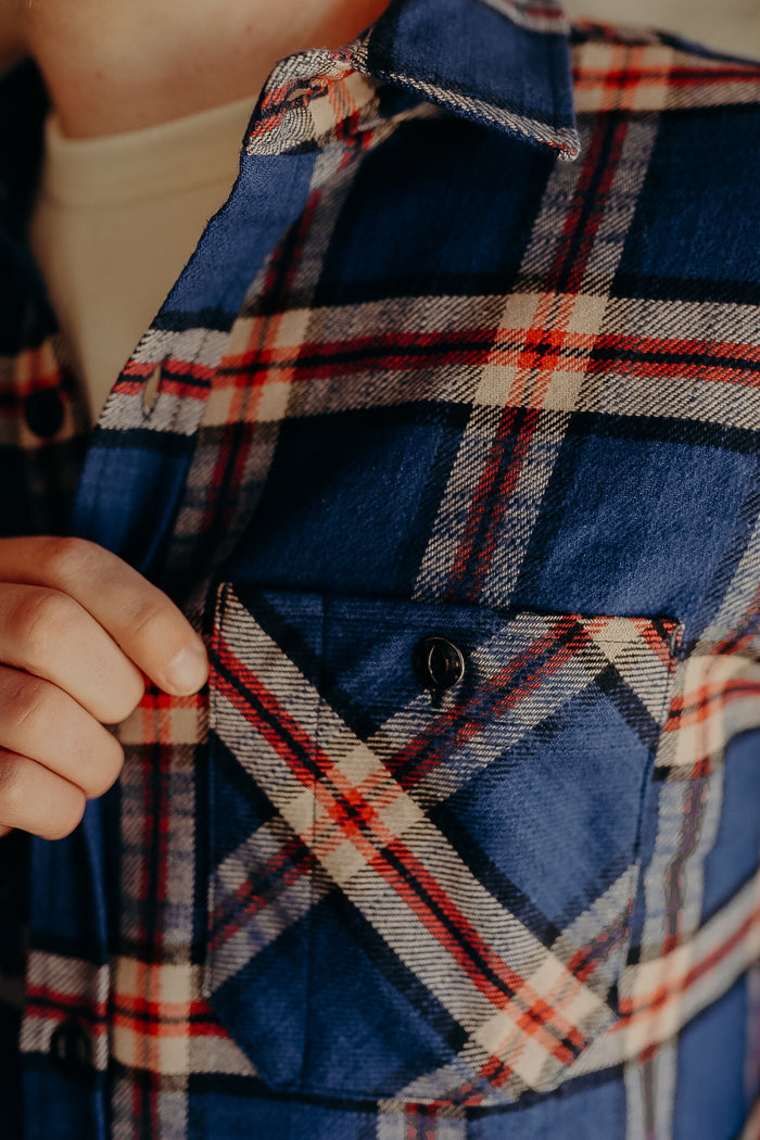 Close-up of hand holding the pocket flap of a blue and red plaid flannel shirt from Iron Shop Provisions