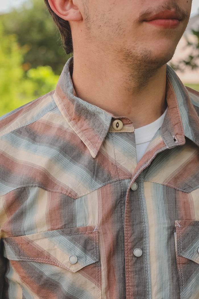Close-up of a person wearing a plaid shirt with a blurred natural background