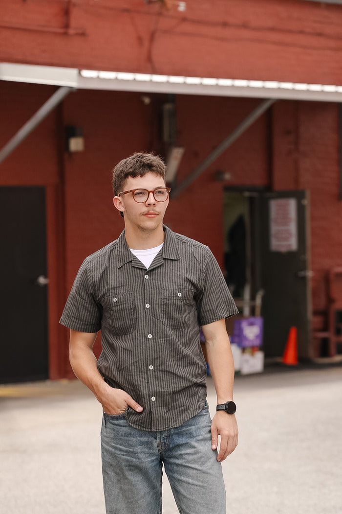 Man wearing a checkered shirt and jeans standing in front of a red building.
